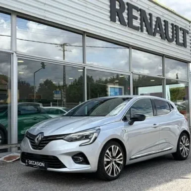 Renault Clio d'occasion argentée devant une concession avec enseigne RENAULT et plaque OCCASION.